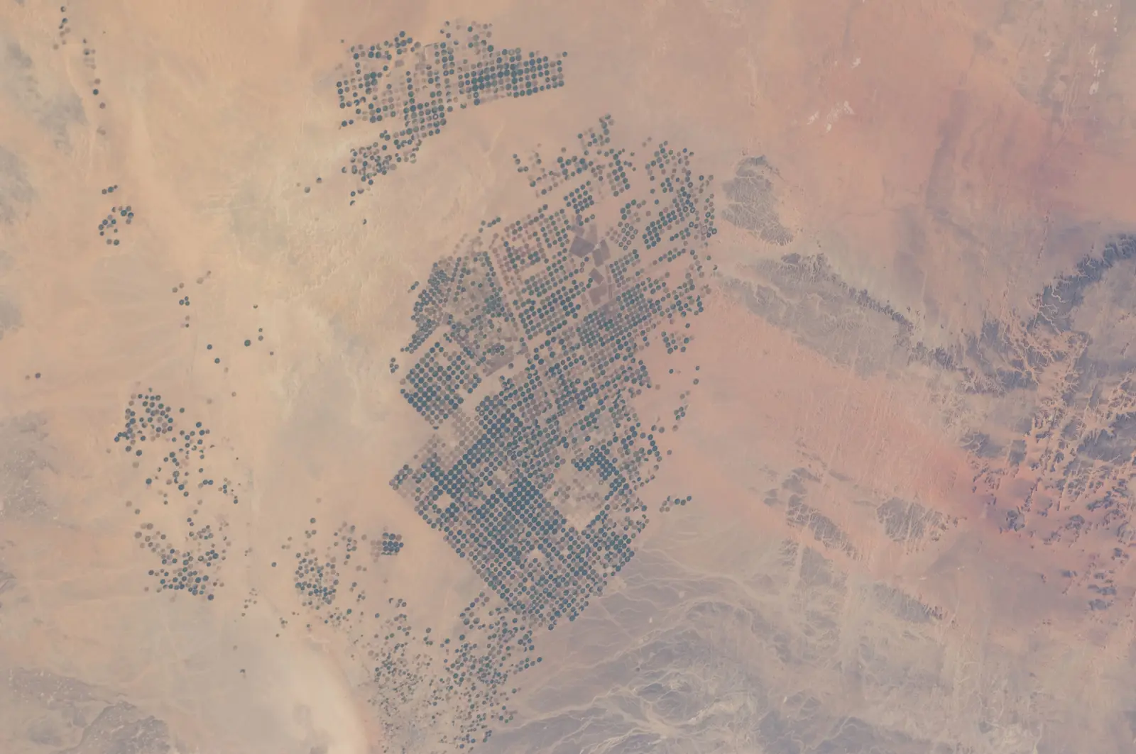 A high-altitude photograph shows a desert landscape featuring numerous clusters of distinct circular patterns. The photographer titled it “Earth Observations taken by Expedition 30 crewmember”.