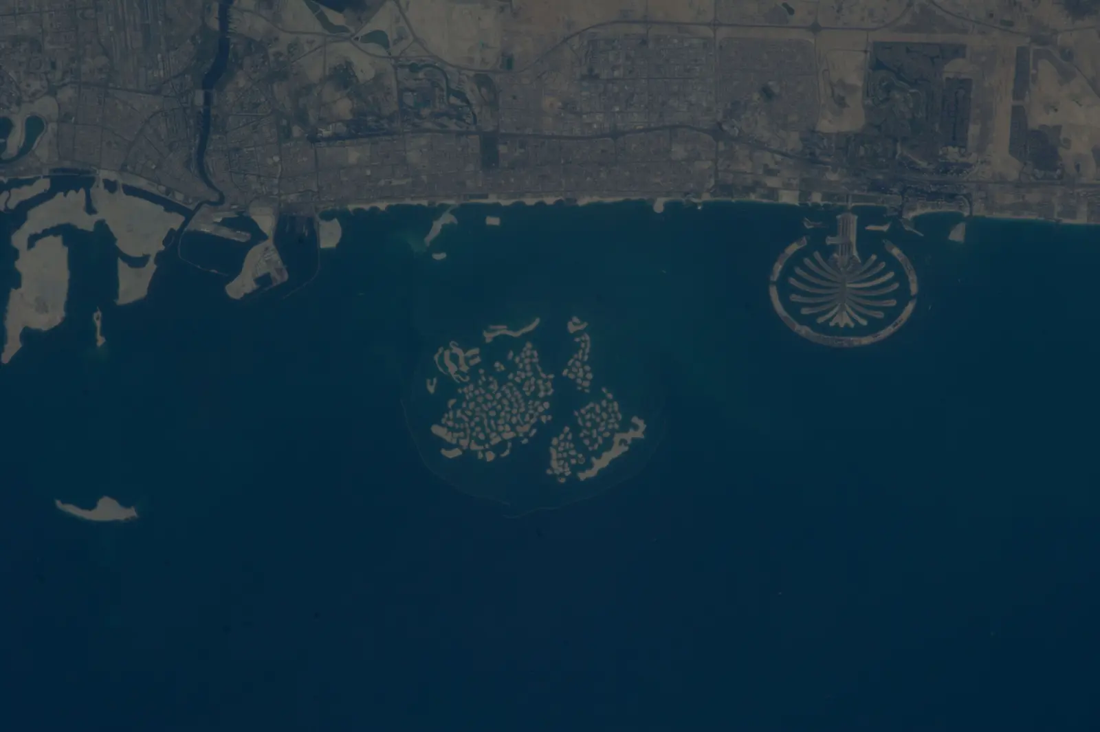 An aerial satellite view shows a coastline with urban infrastructure and several distinct artificial islands in the water. The photographer titled it “Earth Observation”.