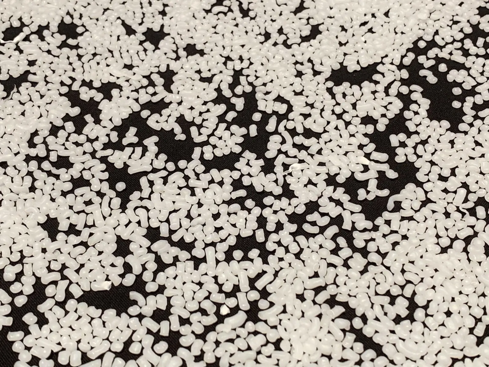 Small white plastic pellets are scattered across a dark background. The photographer titled it “NoPetroPA-plastic-nurdles-public-domain-7787”.