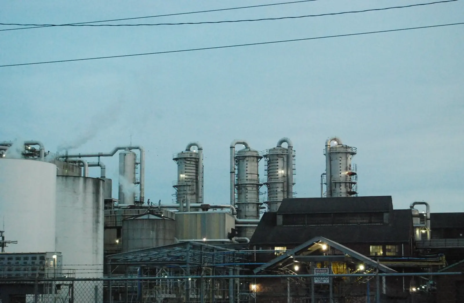 An industrial facility featuring large storage tanks, tall processing towers, and smokestacks releasing steam against a pale sky. The photographer titled it “blue industry”.
