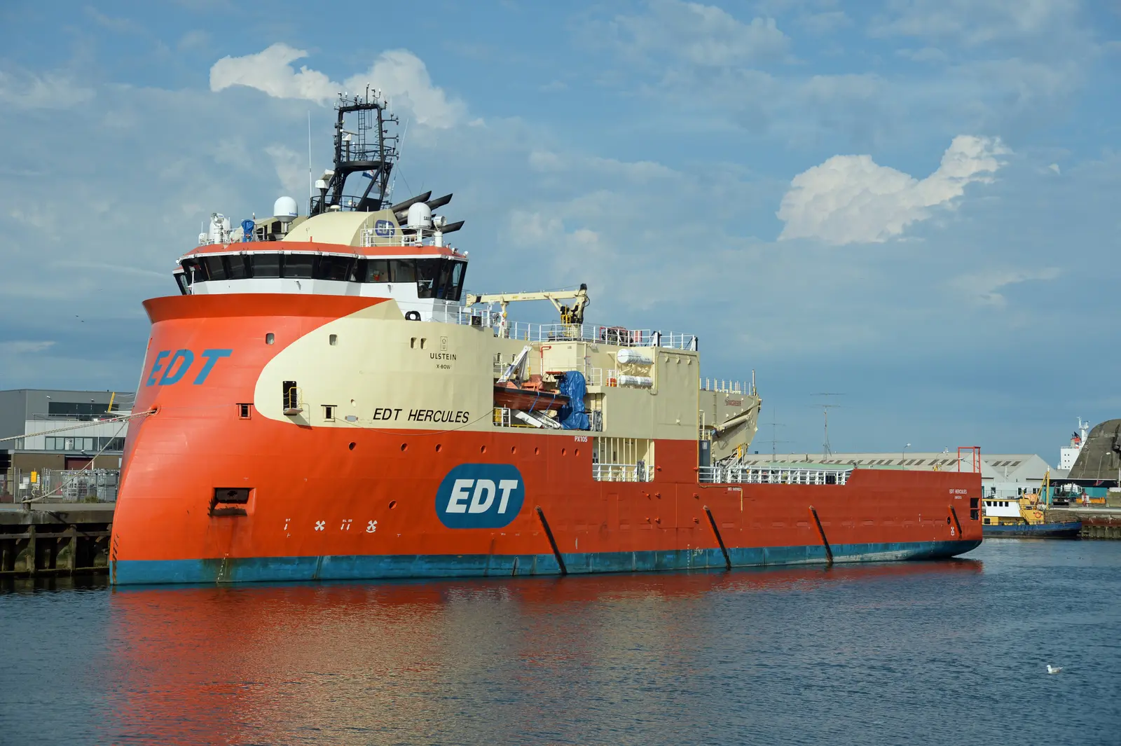 A large red and cream ship with "EDT HERCULES" written on its hull floats in calm water beneath a blue sky with white clouds. The photographer titled it “EDT Hercules IMO 9491422 Offshore Support Vessel”.